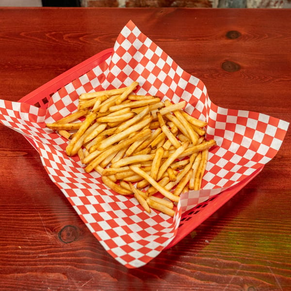 A red basket filled with golden-brown french fries, lined with red and white checkered paper.