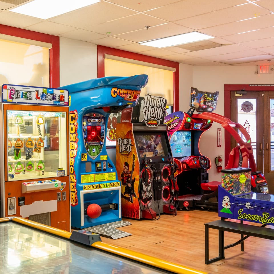 A vibrant arcade room at Corsaro's Family Pizza, featuring various games like Guitar Hero and a prize locker.