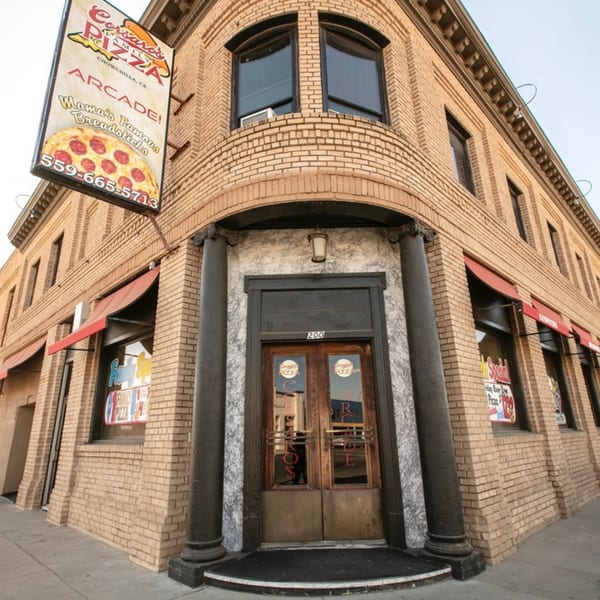 Exterior of Corsaro's Family Pizza, a brick building with red awnings and a large pizza sign.