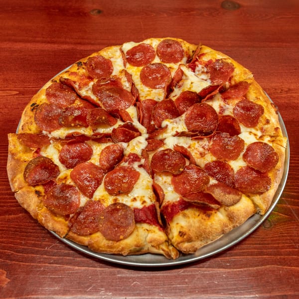 A whole pepperoni pizza, cut into slices, on a metal pan on a rustic wooden table.