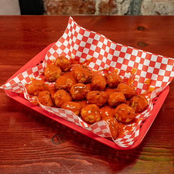 A red basket of Corsaro's boneless wings covered in buffalo sauce on a wooden table.
