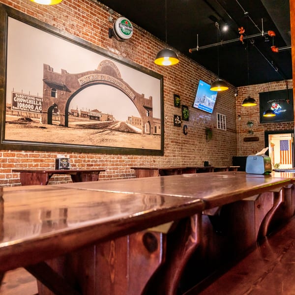 Interior of Corsaro's Family Pizza with brick walls, wooden tables, and a large vintage Chowchilla sign.