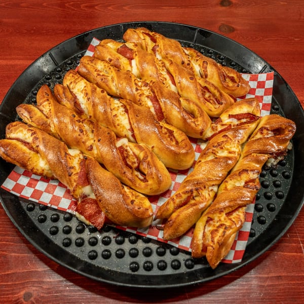A black tray filled with braided pepperoni and cheese breadsticks on red and white checkered paper.