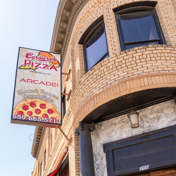 A vertical sign for Corsaro's Family Pizza, featuring a pepperoni pizza, hangs on a brick building.
