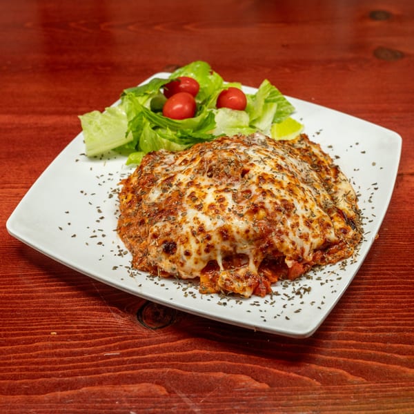 Baked lasagna with melted cheese and herbs, served with a side salad on a white plate.